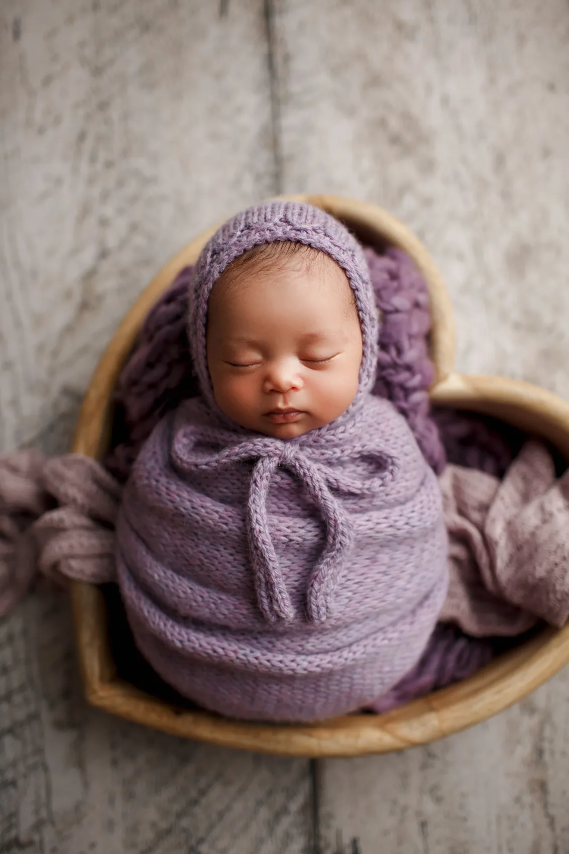 Lavanta renkli örgü bonnet ve kundak içinde, kalp şeklinde ahşap kasede uyuyan bebek